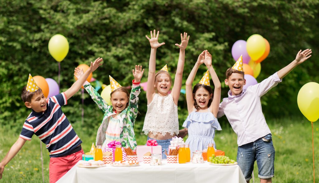 Blije kinderen met feesthoedjes vieren een vrolijk speurtocht kinderfeestje in de tuin, omringd door kleurrijke ballonnen, cadeautjes en een tafel vol snacks tijdens een actief en gezellig verjaardagsfeestje.